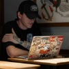 A man wearing a cap working at a computer, managing product images and files for a B2B webshop.