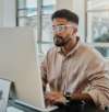 Mann mit Brille arbeitet an einem Desktop-Computer in einer hellen Büroumgebung